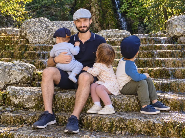 Un père assis avec ses trois enfants sur des marches en pierre